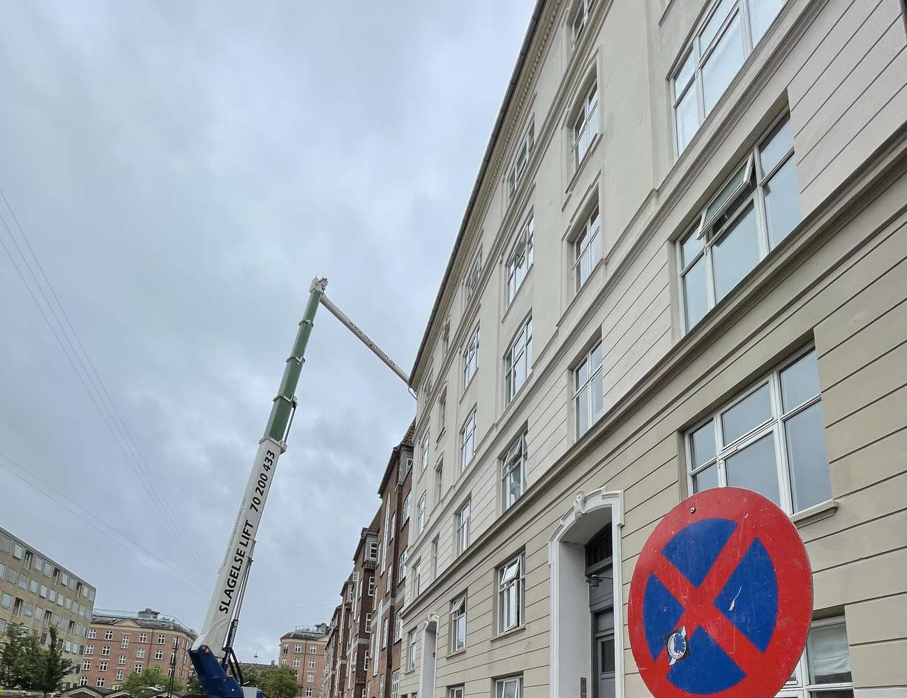 Kran ved en etageejendom under renovering, med skiltning om byggeperioden.
